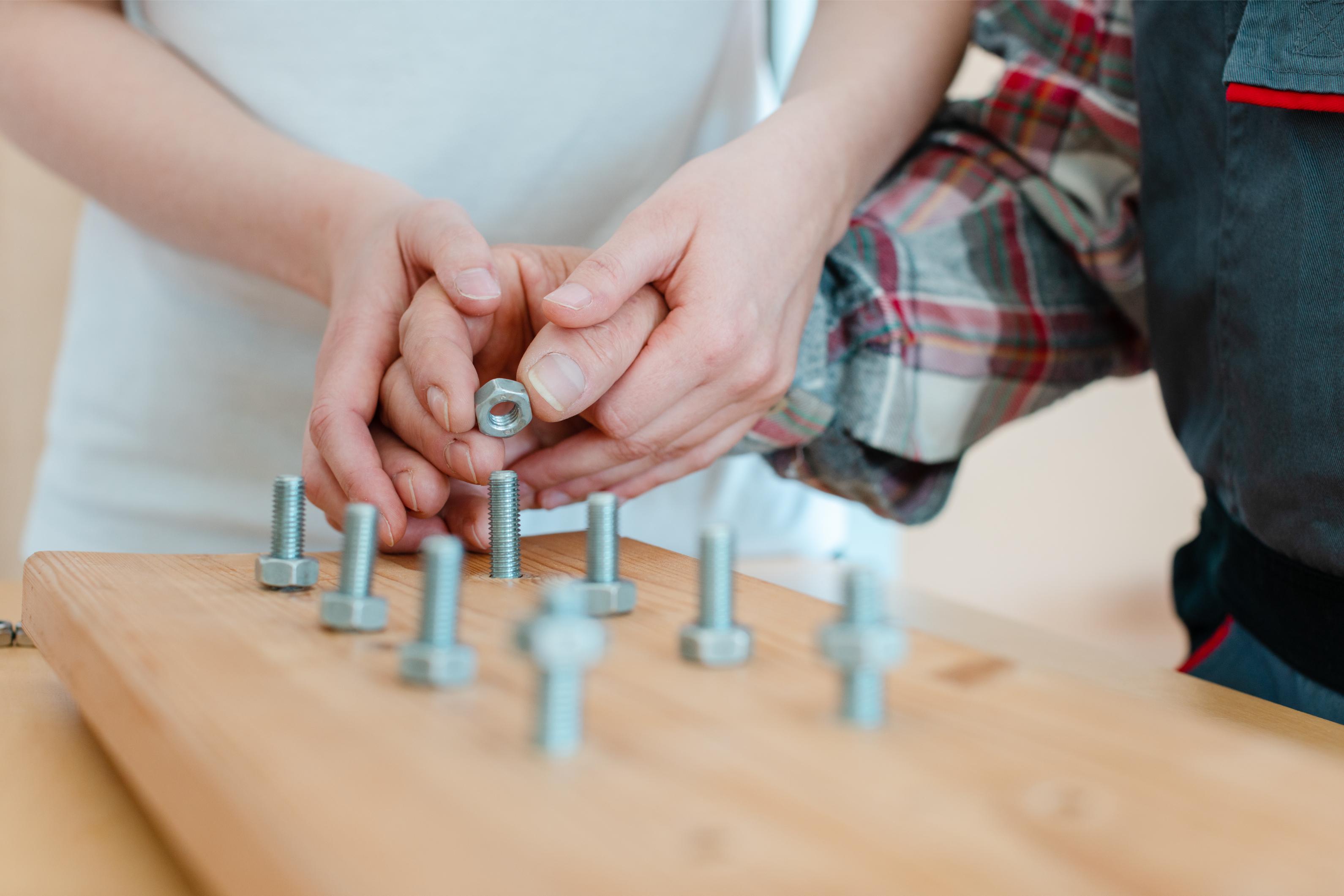 Hände schrauben eine Mutter auf eine Schraube auf einem Holztisch mit mehreren Schrauben.
